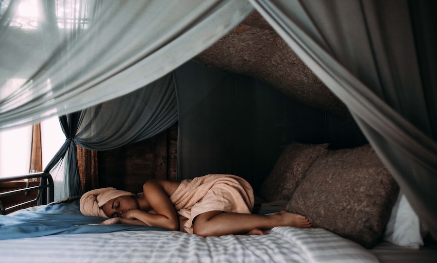 une femme dort paisiblement sur son grand lit baldaquin